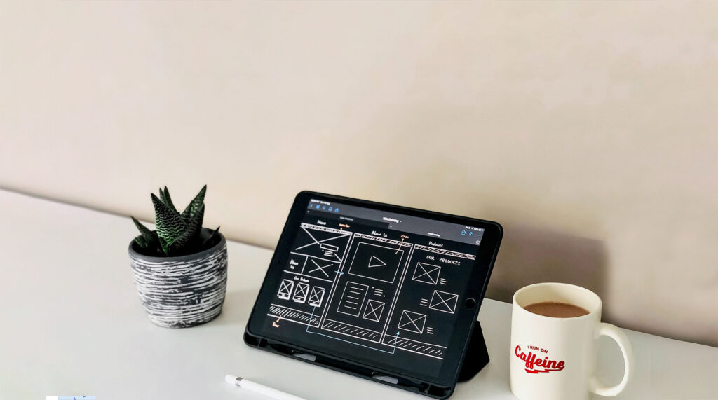 imagen de un laptop con esquema de landing page en la pantalla sobre una mesa con una taza de café