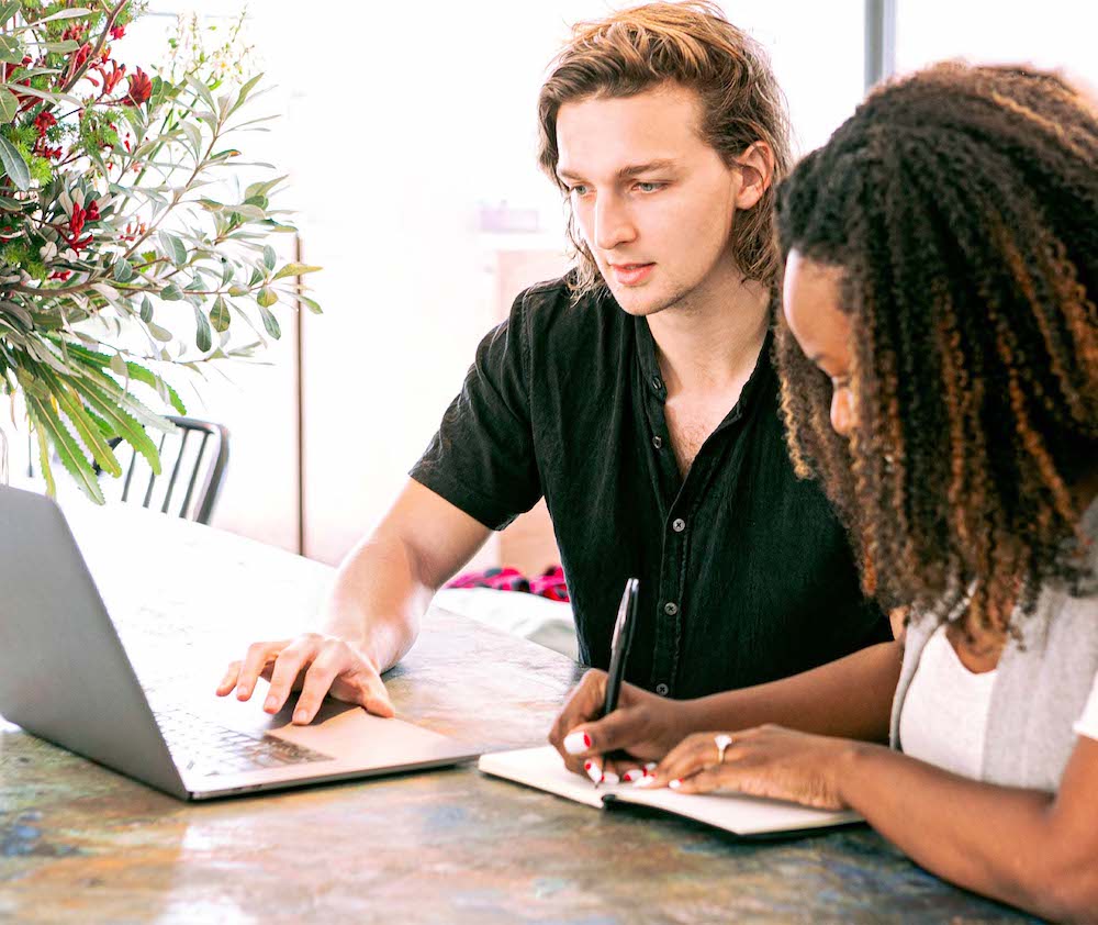 Deux personnes étudient à une table avec un pc et un cahier, la photo illustre un post sur les LMS.