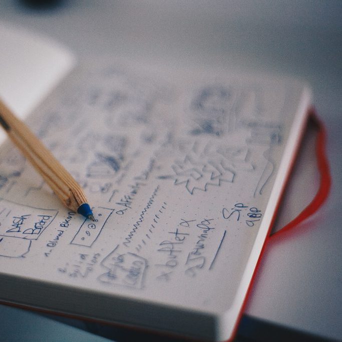 Libreta con notas y dibujos escritos a mano, con un lápiz encima, en post sobre cómo crear un pitch