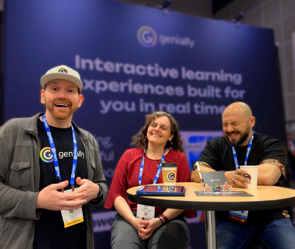 Three Genially team members smile and chat around a table at ATD event booth, with the message “Interactive learning experiences built for you in real time” displayed in the background.